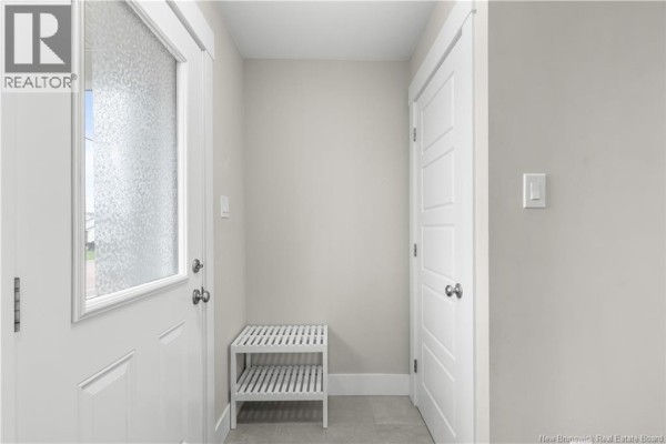Interior view of a bright entryway with light grey walls, a white door, and a white slatted shoe rack. - 51-53 Macintosh Boulevard, Moncton