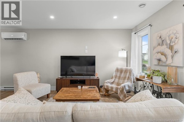 Living room features a large television, sofas, a wooden coffee table, and artwork on the light grey walls. - 51-53 Macintosh Boulevard, Moncton