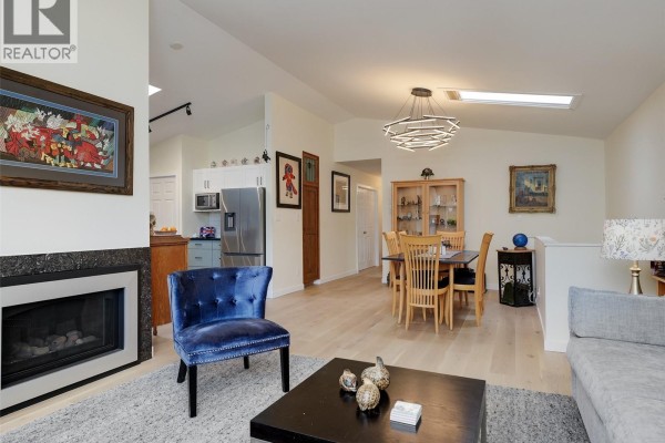 Living and dining area with a fireplace, blue accent chair, dining table with wooden chairs, and a skylight. - 51 901 Kentwood Lane, Saanich