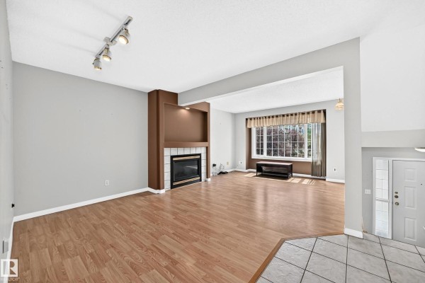 Living room with wood laminate flooring, a brown fireplace, and a large window. - #51 9630 176 St Nw, Edmonton