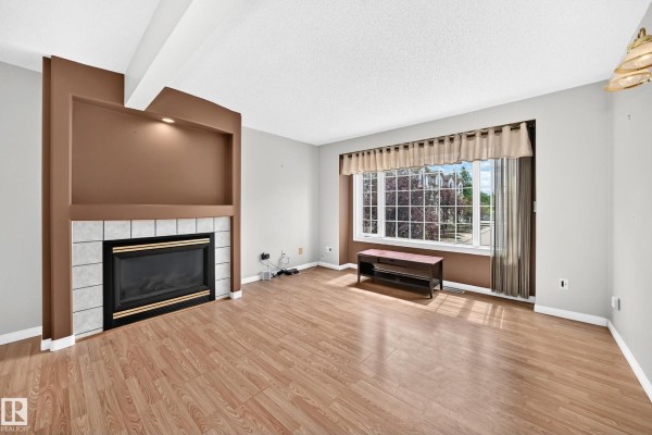 Living room featuring a gas fireplace, wood laminate floors, and a bay window. - #51 9630 176 St Nw, Edmonton