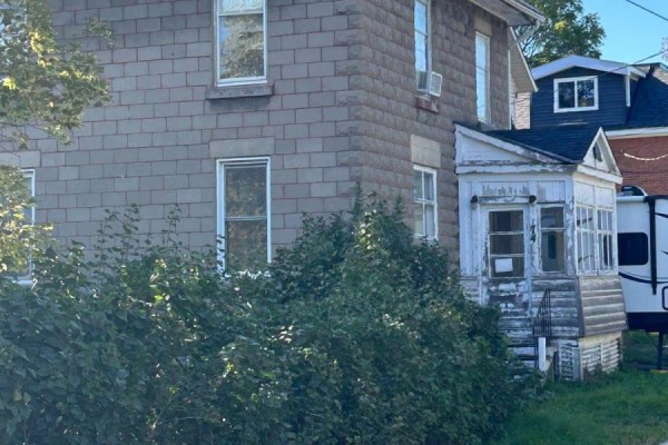 Exterior view of the stone house with overgrown bushes in the foreground. - 51 Albert Street, Carleton Place
