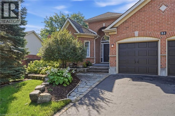 Close-up of the front entrance of a red brick house with a stone walkway and lush landscaping. - 51 Autumn Ridge Trail, Kitchener