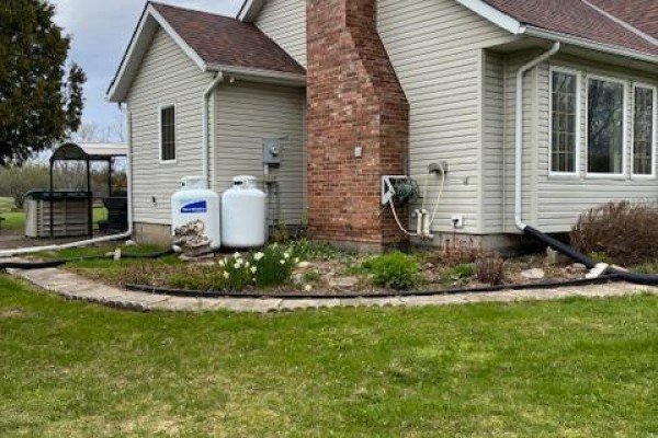 Detail of the brick chimney and propane tanks next to the house with green grass and plants. - 51 B Jericho Road, Prince Edward County