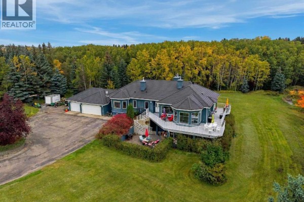 Exterior of a blue house with a white deck and attached garage, surrounded by green lawns and trees. - 51 Blueridge Close, Rural Rocky View County