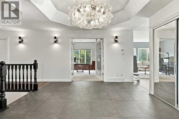 Interior foyer with dark grey tile floors, a large crystal chandelier, and double doors leading to an office. - 51 Blueridge Close, Rural Rocky View County