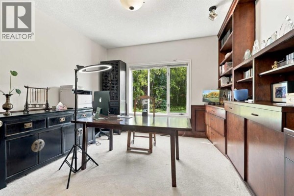Home office with a large dark wood desk, built-in bookshelves, and a window overlooking greenery. - 51 Blueridge Close, Rural Rocky View County