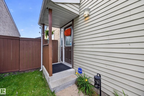 Covered front porch with a brown door, mat, and a hanging wreath. Concrete steps and siding. - 51 Chungo Dr, Devon