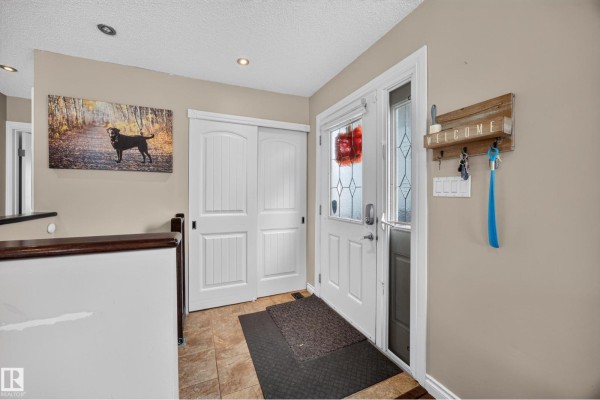 Foyer with a front door, double white closet doors, tiled floor, and beige walls. Artwork on wall. - 51 Chungo Dr, Devon