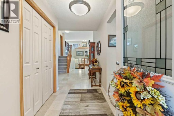 Entryway with tile flooring, double bi-fold closet doors, staircase, and entryway table. - 51 Douglasbank Gardens Se, Calgary