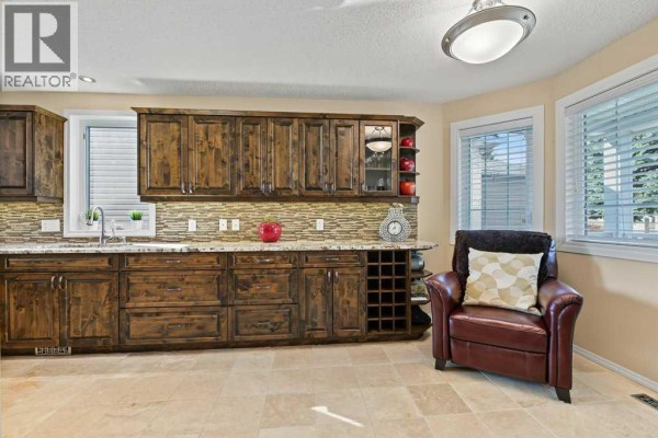 Kitchen with dark wood cabinets, granite countertops, tiled backsplash, wine rack, and leather armchair. - 51 Douglasbank Gardens Se, Calgary