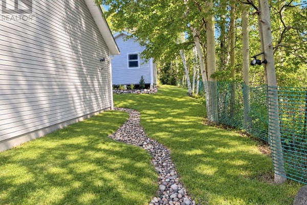 Pathway of smooth stones meandering through the green lawn between the house and a wooded area. - 51 Main Street, Hare Bay