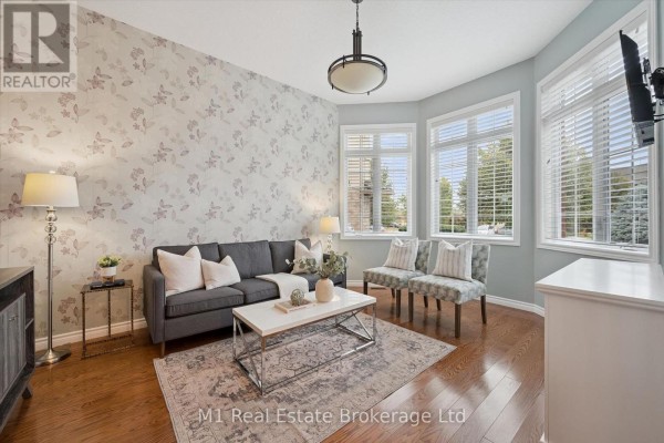 Living room with a grey sofa, patterned accent chairs, bay windows, and hardwood floors. - 51 Mcgowan Street, Centre Wellington