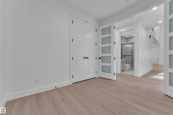 Interior room with white walls, light wood floors, double doors, and a view into a bathroom with a tiled shower. - 51 Meadowgrove Lane, Spruce Grove