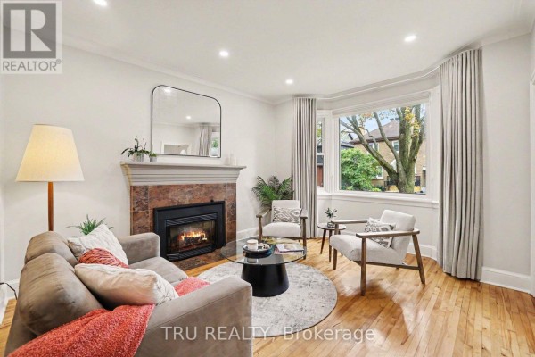 Living room with a fireplace, sofa, chairs, round rug, and bay window. - 51 Merritt Avenue, Ottawa