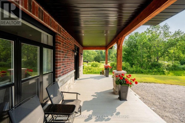 View of the covered front porch from the side, showing seating and the exterior brickwork. - 51 Morrow Road, Trent Hills