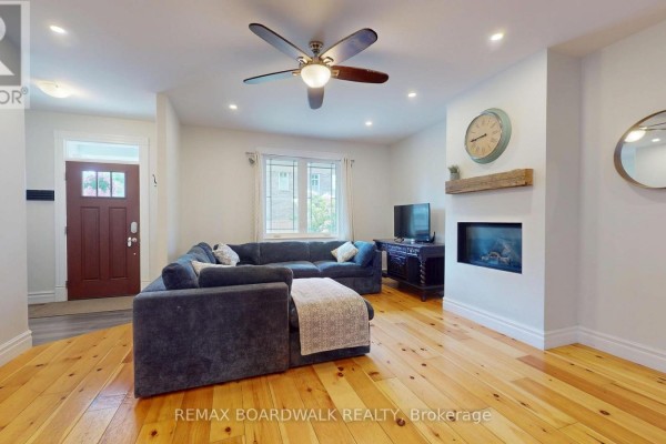 Living room with a sectional sofa, fireplace, television, and wooden floors. - 51 Ormond Street, Brockville