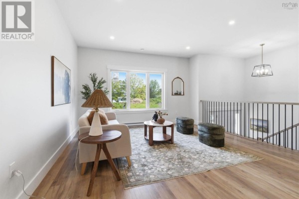 Living room space with light wood floors, a patterned area rug, sofa, and large window view. - 51 Pine Hill Drive, Elmsdale