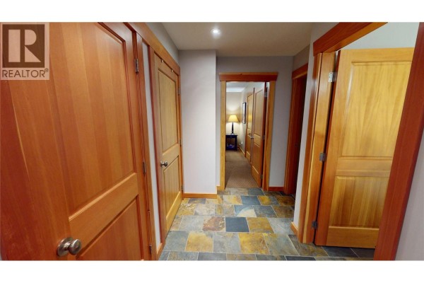 Hallway with slate tile floor and multiple closed wood doors. - 51 Rivermount Place Unit# 103, Fernie