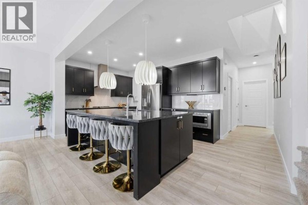 Kitchen island with grey tufted bar stools and a view of the stairs and artwork. - 51 Setonstone Row Se, Calgary