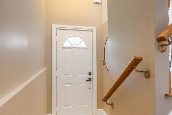 Interior hallway with a white door featuring arched glass, wooden banister, and beige walls. - 51 Spadina Road, Brampton