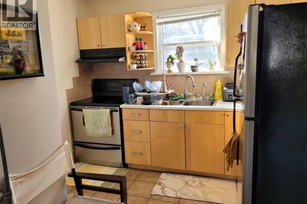 Kitchen counter with black stovetop, oven, double sink, light wood cabinets, and stainless steel refrigerator. - 51 Talbot Street, Kitchener