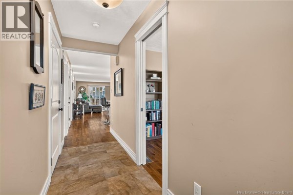 Hallway interior with tan walls, tile floor, and doors leading to rooms and a bookshelf. - 51 Thornhill Crescent, Moncton