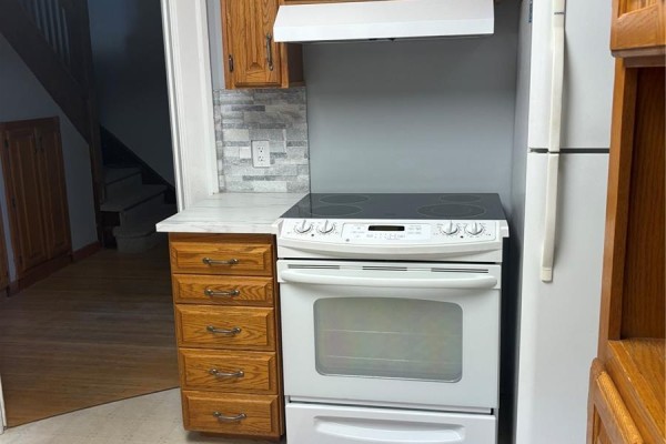 Kitchen with oak cabinets, white stove and refrigerator, and a frosted glass door. - 51 Tupper Avenue, Yorkton