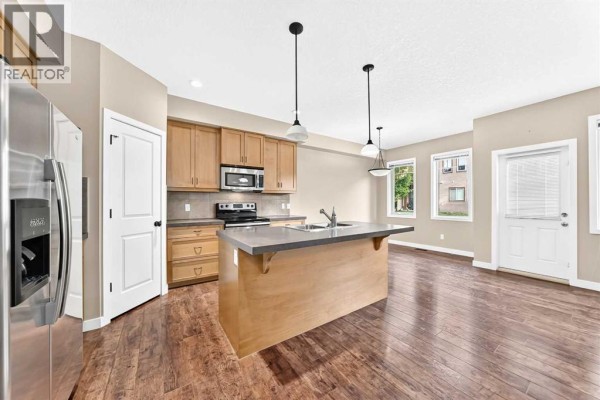 Open-concept kitchen and living area with island, refrigerator, and backyard view. - 510, 413 River Avenue, Cochrane