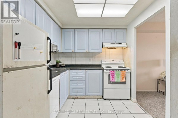 L-shaped kitchen with light blue cabinets, white appliances, black countertops, and white tiled floor. - 510 - 135 Hillcrest Avenue, Mississauga