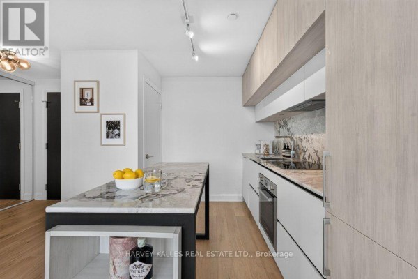 Kitchen with island, white cabinets, light wood finishes, and stainless steel appliances. - 510 - 151 Avenue Road, Toronto