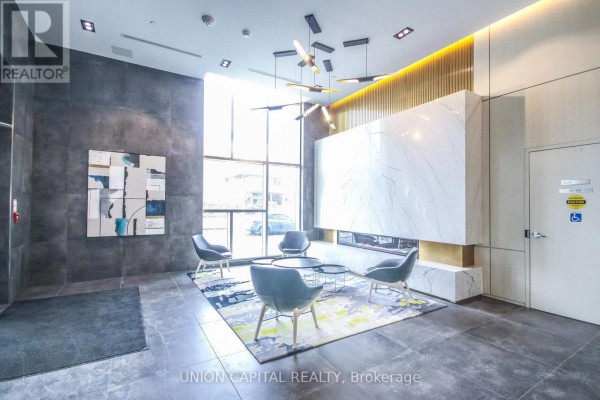 Lobby seating area with grey chairs, fireplace, and large windows overlooking the street. - 510 - 223 St Clair Avenue W, Toronto