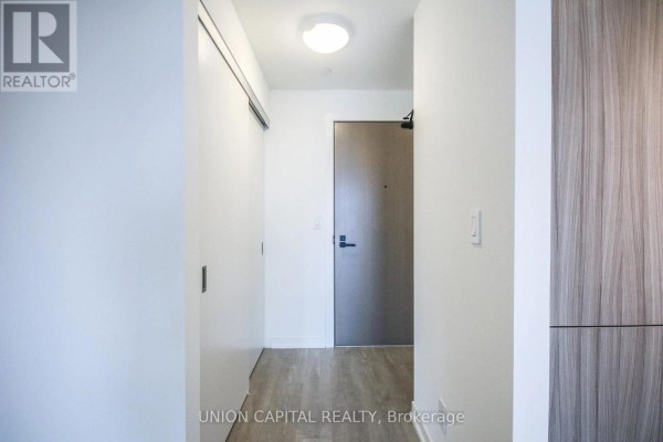 Hallway with white walls, light wood flooring, and a dark grey door. - 510 - 223 St Clair Avenue W, Toronto