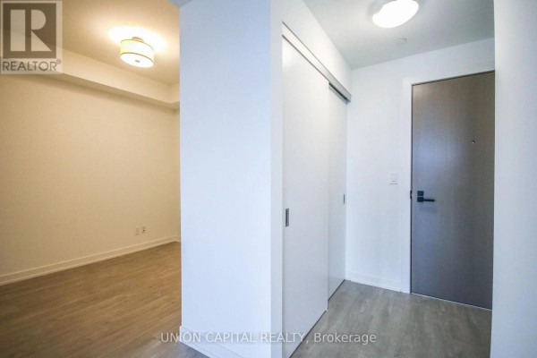 Apartment hallway with white walls, grey door, and view into a room with wood floors. - 510 - 223 St Clair Avenue W, Toronto