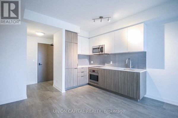Modern kitchen with two-tone cabinets, stainless steel appliances, and grey backsplash. - 510 - 223 St Clair Avenue W, Toronto