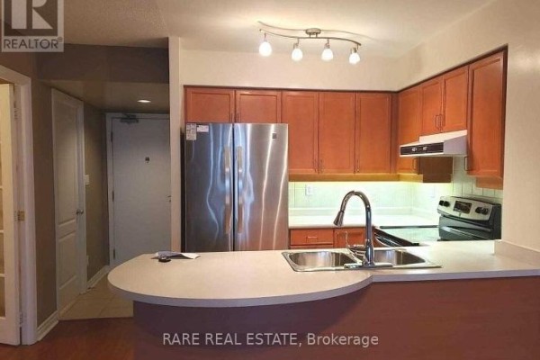 Kitchen with wood cabinets, stainless steel refrigerator, and a breakfast bar with sink. - 510 - 3 Rean Drive, Toronto