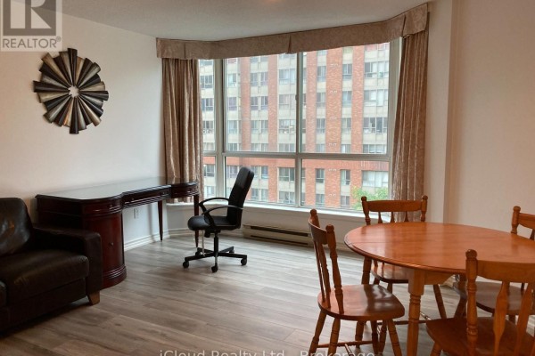 Living and dining area with a bay window, wooden table, chairs, desk, and leather armchair. - 510 - 38 Elm Street, Toronto
