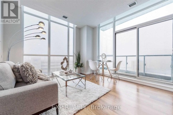 Living area with a grey sofa, glass coffee table, white rug, and dining nook. - 510 - 70 Forest Manor Road, Toronto