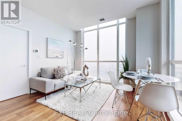 Living room with a sofa, glass coffee table, and round dining table near a large window. - 510 - 70 Forest Manor Road, Toronto