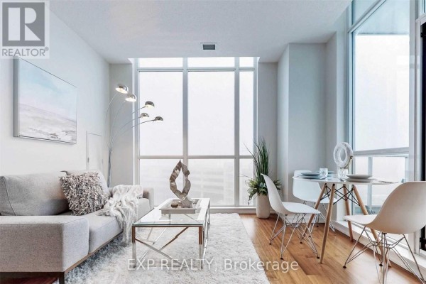 Living and dining area with large windows, a grey sofa, and a modern dining set. - 510 - 70 Forest Manor Road, Toronto