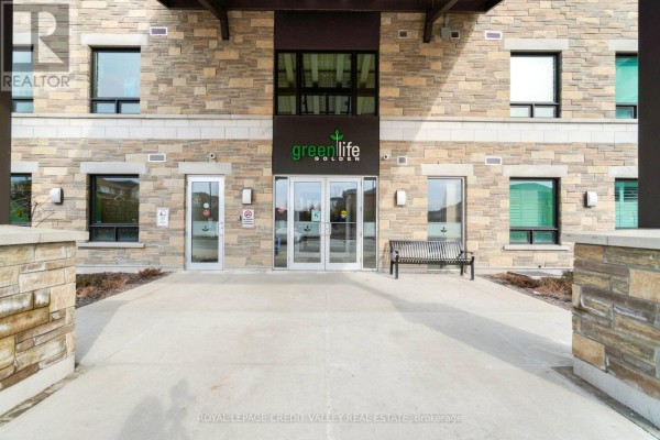 Close-up of the building entrance with glass doors, stone accents, and a bench on the concrete walkway. - 510 - 7400 Markham Road, Markham
