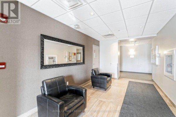 Building hallway with two black leather armchairs, a large mirror on the wall, and tiled flooring. - 510 - 7400 Markham Road, Markham