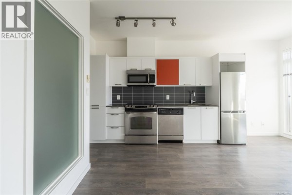 Kitchen with stainless steel appliances, white cabinets, and a glimpse of a frosted glass partition. - 510 517 Fisgard St, Victoria