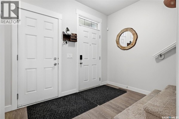 An open-concept living area with dark wood floors, a kitchen island with chairs, and a living room. - 5101 Tutor Way, Regina