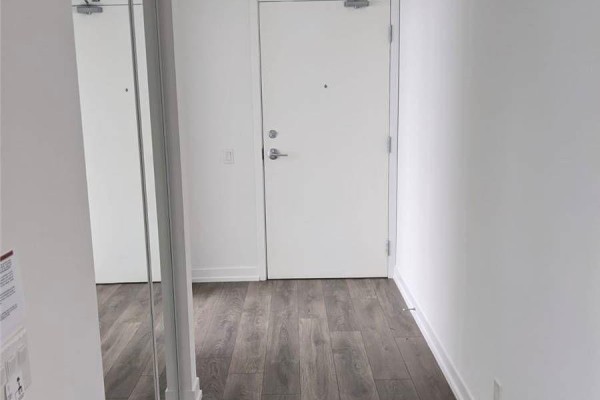 Hallway with grey wood laminate flooring, a large mirror, and a white interior door. - 5102 - 5 Buttermill Avenue, Vaughan