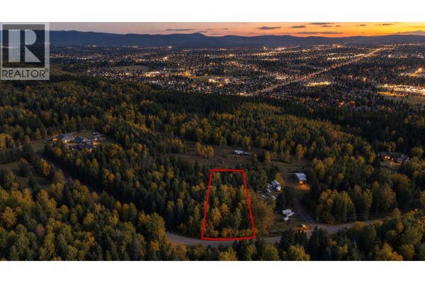 Dusk aerial view of a treed lot outlined in red, overlooking the illuminated Prince George cityscape. - 5102 Cranbrook Hill Road, Prince George