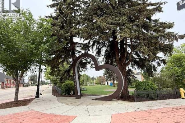 Street view of 50 Avenue, Lacombe, showing buildings, trees, and a distant cell tower. - 5105 50 Avenue, Lacombe