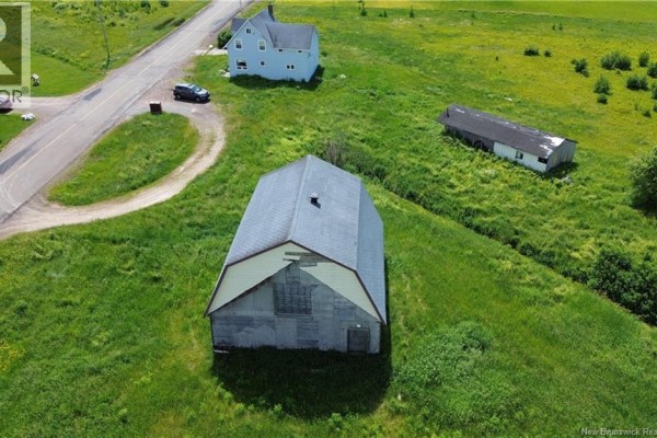 Aerial view of a large barn in a green field with a light blue house and a road visible. - 5106 Route 495, Sainte Marie De Kent
