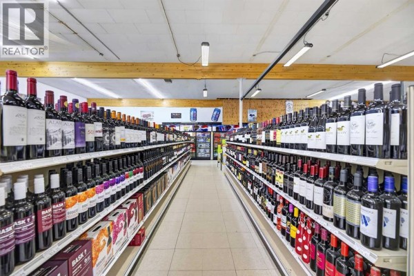 View down an aisle of a store, with shelves stocked full of wine bottles and boxes on both sides. - 5107 50 Avenue, Olds