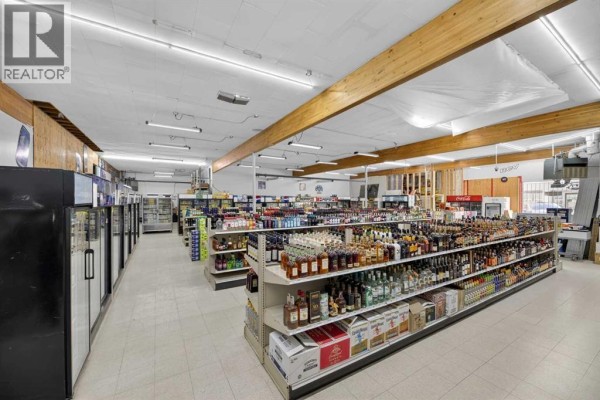 Interior view of a retail store with aisles of shelves stocked with beverages and refrigerators along the wall. - 5107 50 Avenue, Olds